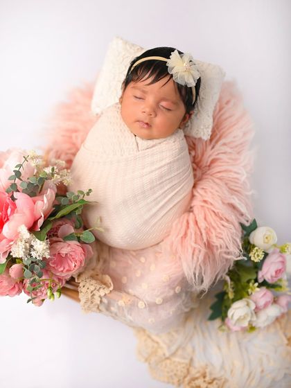 A newborn baby girl sleeps peacefully in a cozy pink setup, surrounded by beautiful peonies. I love using floral elements in my newborn photography.
