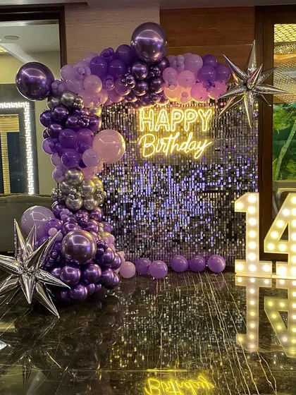 This is a duplicate of ID 64, 115, 129, 159, 196. A glamorous 14th birthday setup with a purple shimmer wall. This decoration features a stunning organic balloon garland in shades of purple and silver, a 'Happy Birthday' neon sign, and large marquee numbers.