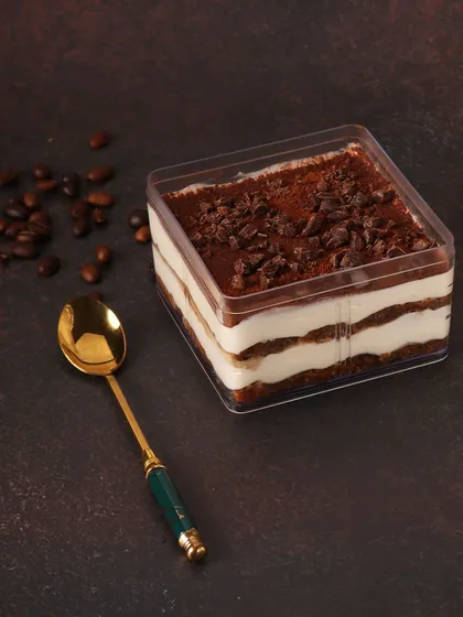 Our Tiramisu dessert tub, showing the beautiful layers of coffee-soaked ladyfingers and creamy mascarpone, dusted with cocoa powder. It's a classic Italian dessert, perfect for a cozy indulgence.
