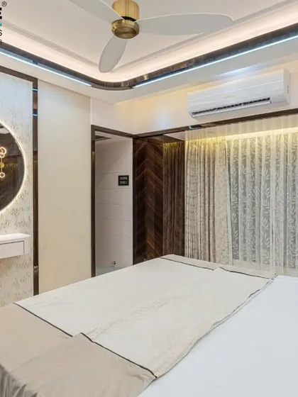 A bright and elegant bedroom in Seawoods with a large, backlit circular mirror that doubles as a vanity. The design uses a light color scheme with dark wood accents for a modern, high-contrast look.