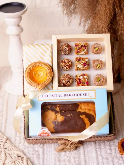 A close-up of the 'Pure Indulgence Hamper', showcasing the beautiful textures of the jute basket, the earthen diya, and our freshly baked tea cake.