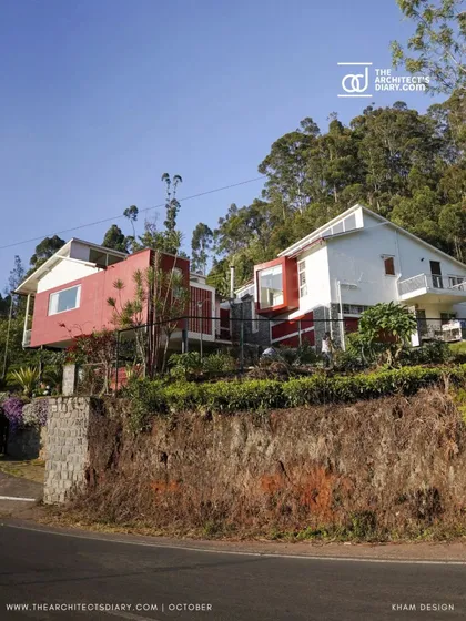 The bold red and white volumes of the farmhouse stand out against the green landscape. The design uses simple geometric forms that are stacked and arranged to follow the land's contours.