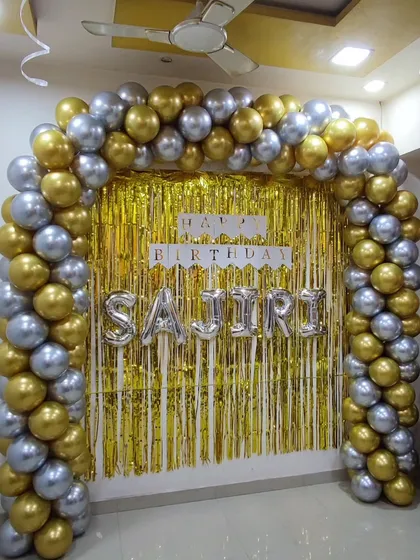 A glamorous gold and silver balloon arch frames a gold shimmer curtain. This setup, personalized with the birthday person's name in silver foil letters, creates a luxurious and festive party entrance.