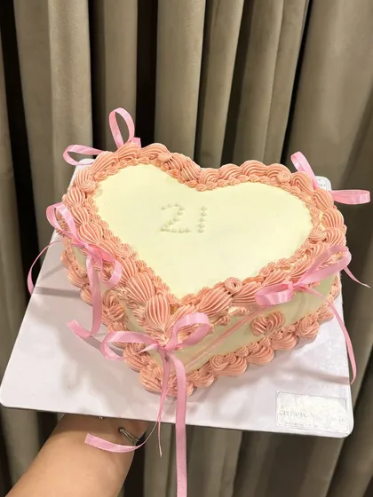 For the love of vintage charm. This heart-shaped cake features intricate Lambeth piping and delicate ribbon bows, perfect for celebrating a 21st birthday with a touch of classic elegance.