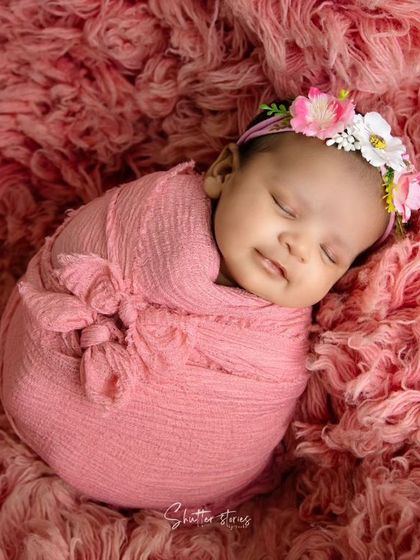 A smiling baby in a pink wrap on a matching textured rug. This shows how to create a simple yet impactful monochromatic setup.