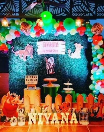 A Lion King 'Wild One' party theme with a dark, moody feel, using a grass wall and character cutouts of Simba, Timon, and Pumbaa.