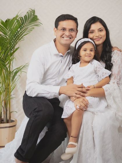 A picture of a happy family. Dressed in coordinating white outfits against a bright, boho-inspired backdrop, their smiles radiate warmth and love. This is what a perfect family portrait feels like.