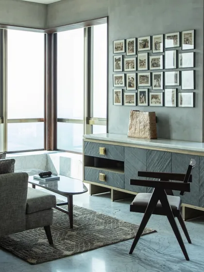 A seating area within the master bedroom, featuring a chair by Pierre Jeanneret and a custom console in stone veneer and brass. The space is personalized with a gallery wall of family photos.