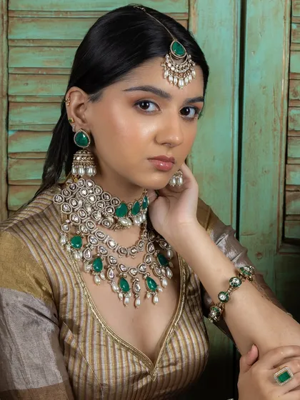 This bridal set features layered Kundan necklaces with emerald drops and delicate pearls, paired with matching jhumka earrings and a maang tikka. It's a complete look that exudes grace and sophistication for the modern bride.