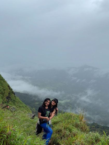 Two friends posing on the Gangadikal trail with the vast, misty landscape behind them.