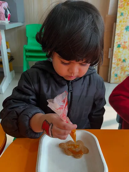 A little boy carefully pipes icing onto his cookie, showing great concentration.