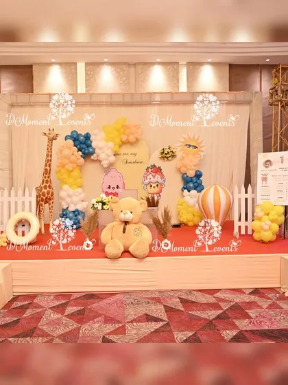 The main stage for the twins' celestial-themed first birthday. The setup includes a large teddy bear, animal props, a hot air balloon cutout, and balloon garlands against a simple, elegant backdrop.