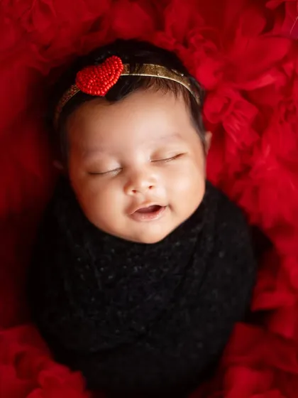A close up of this beautiful baby girl, capturing a soft, sleepy smile. The contrast of the black wrap and red background is stunning.