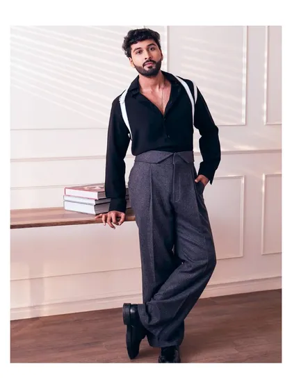 A bold look featuring a black shirt with unique white strap details, paired with high waisted grey trousers. This is for the man who isn't afraid to experiment with style.
