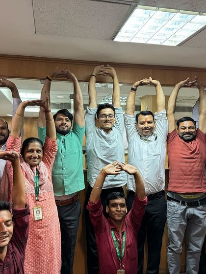 A happy group of employees at SMC Global making a heart shape with their arms. These sessions are not just about yoga; they are about team bonding and boosting morale.