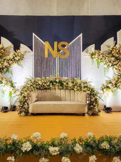 A wider perspective of the 'NS' monogram stage, showing how the elements come together. The design features a navy blue backdrop, white paneled wings, and asymmetrical floral arrangements for a contemporary yet balanced look.