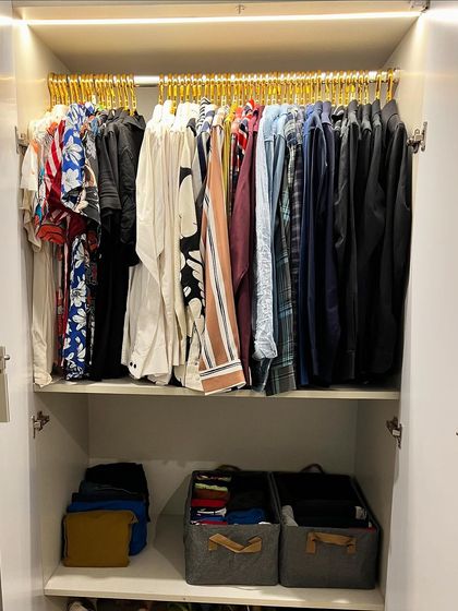 A clean and simple men's wardrobe using matching gold hangers for shirts and grey baskets for folded items, creating a uniform and stylish look.