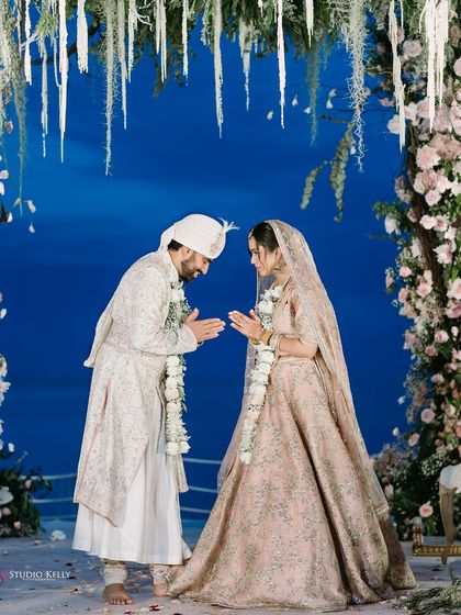 The couple greets each other with a traditional 'namaste' under their floral mandap, a moment of respect and love during their Thailand wedding.