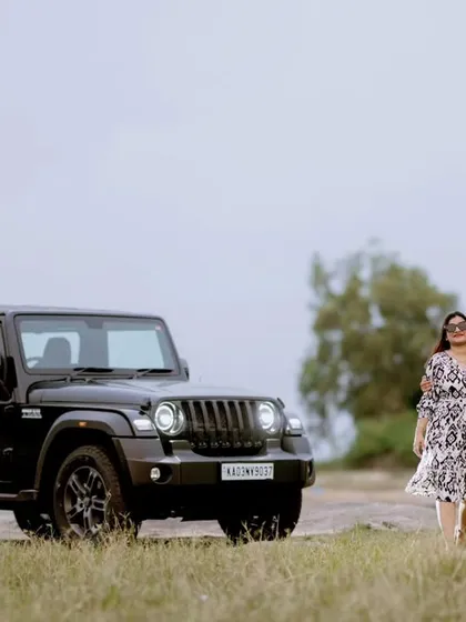 A stylish couple walks hand-in-hand next to a black Mahindra Thar, set against a rustic, open landscape. This image is for adventurous couples looking for a bold, road-trip-themed shoot.