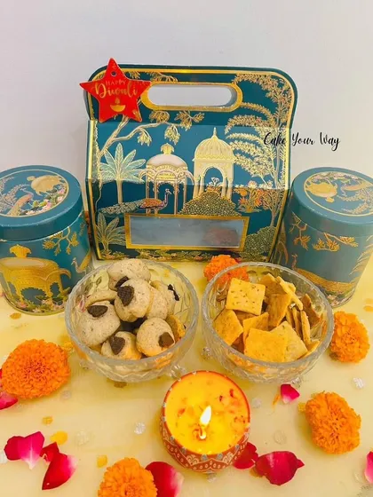 The 'Diwali Dastaan' Gift Hamper is a premium offering in elegant packaging. This option includes two tins filled with treats like Peanut Butter Mini cookies and Cheesy Snack Bites.