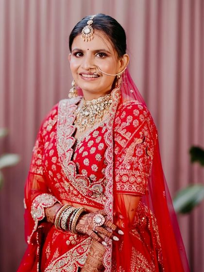 A full-length portrait of the bride in a classic red lehenga. The makeup is balanced to look beautiful in both close-up and full-length photos.