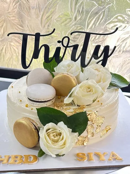Thirty has to be special! An elegant white and gold cake for a 30th birthday, decorated with fresh white roses, macarons, and gold leaf.