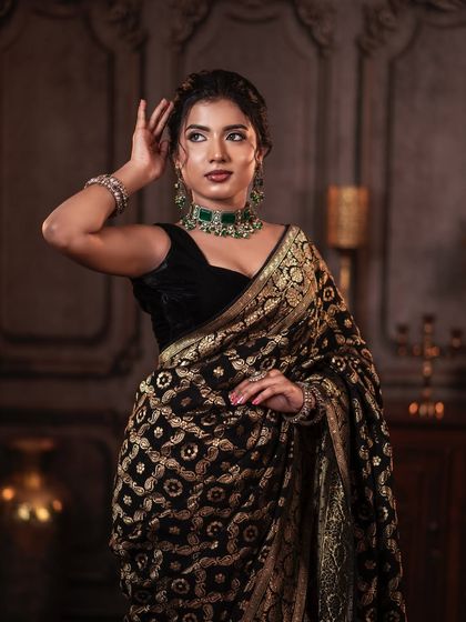 A full-length shot of the elegant black and gold saree look. The messy bun adds a touch of modern sophistication.