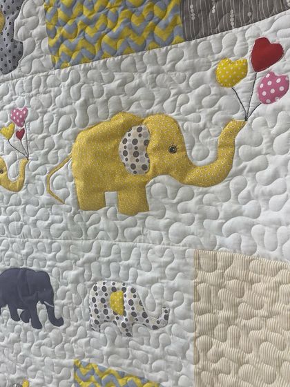 A close-up of a yellow elephant holding heart-shaped balloons, a sweet detail on this baby quilt.