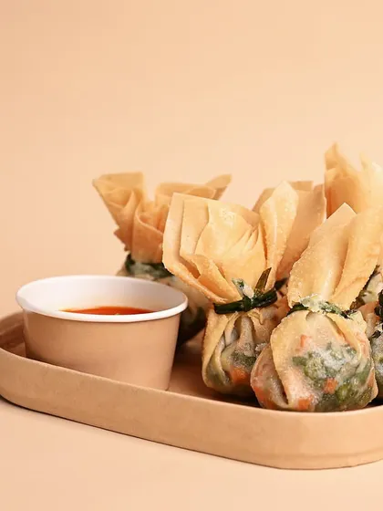 A serving of our crispy Money Bags, filled with finely chopped vegetables and tied into a distinctive pouch shape. They are served with a tangy dipping sauce, perfect for starting your meal.