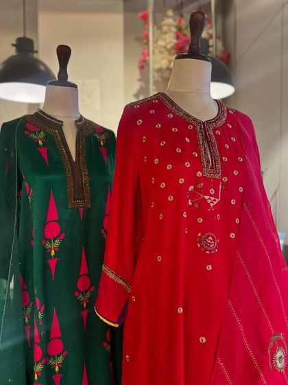 Two festive kurta sets in emerald green and bright red, featuring intricate embroidery and mirror work, perfect for wedding celebrations.