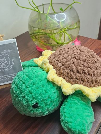 A sunflower turtle made with soft plush yarn, sitting next to a plant.