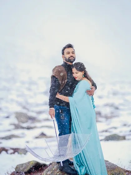 A romantic portrait of a couple embracing in the snow. The bride's light blue saree contrasts beautifully with the white landscape, creating a visually striking and emotional image.