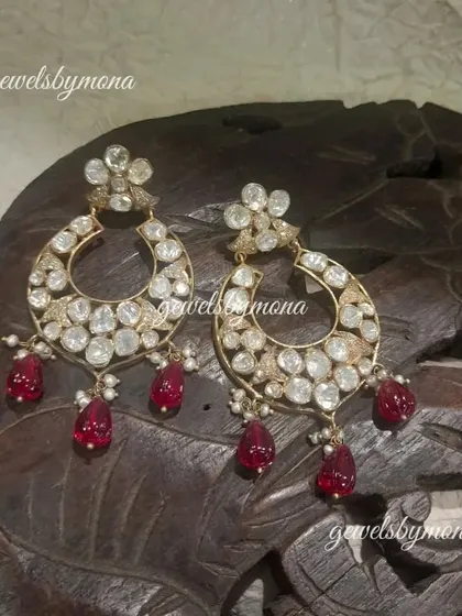 These polki chandbali earrings are a classic design, elevated with beautiful ruby drops. The crescent shape is filled with sparkling polki stones, making them a perfect accessory for weddings and festive occasions.