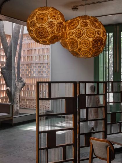 The warm glow from the large, handcrafted pendant lights creates a focal point in the room. In the background, a tree is visible through a window, reinforcing the connection to nature.