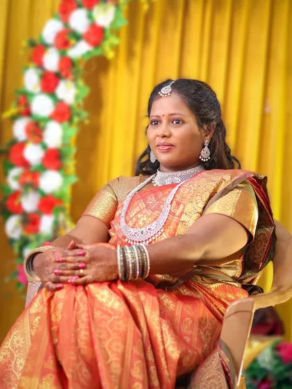 A poised and elegant portrait of the bride seated during her wedding reception. The soft lighting highlights her beautiful orange and gold saree and the intricate diamond jewellery she is wearing.