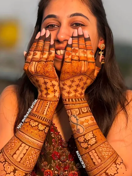 A happy client showing off her beautiful mehndi, which includes a heart and infinity symbol for her engagement.