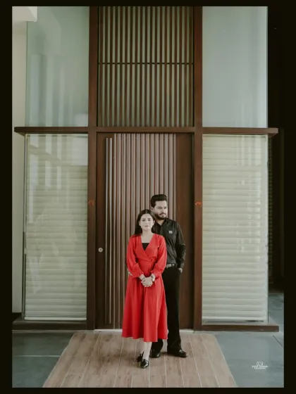 A formal, full-length portrait of a couple standing before a modern wooden and glass door, exuding elegance and sophistication.