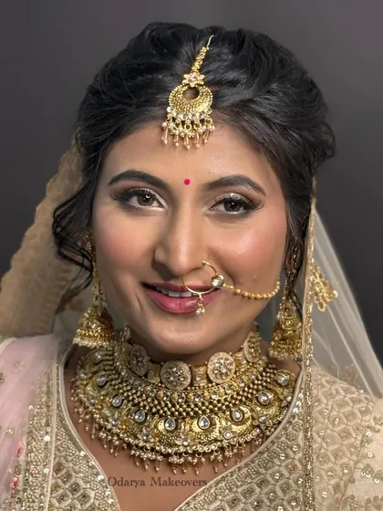 A classic bridal portrait. The makeup is balanced, with defined eyes and a soft lip, allowing the heavy jewellery and outfit to take center stage while still highlighting her features.