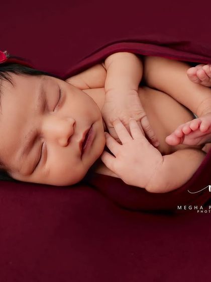 A close-up of a sleeping newborn in a deep red wrap, highlighting their perfect features and peaceful expression. This is a classic newborn portrait.