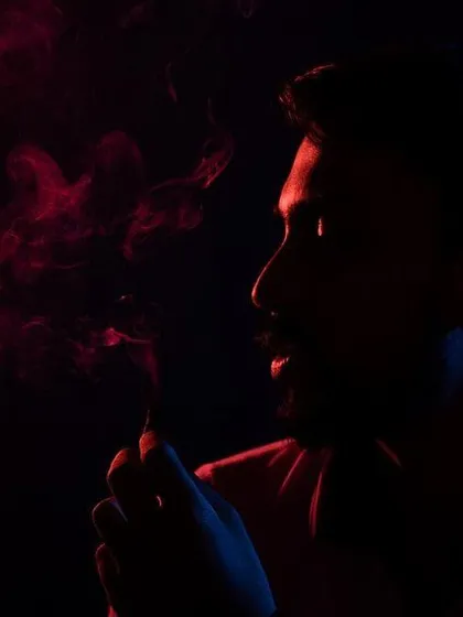 A moody and atmospheric portrait using low-key lighting. The combination of red and blue light with smoke creates a cinematic feel, sculpting the subject's profile against the dark background.