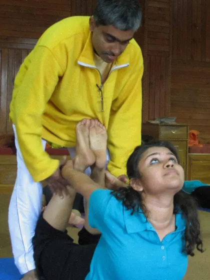 A teacher helps a student deepen their bow pose. This kind of partner assistance is a key learning tool for aspiring teachers to understand anatomy and alignment.
