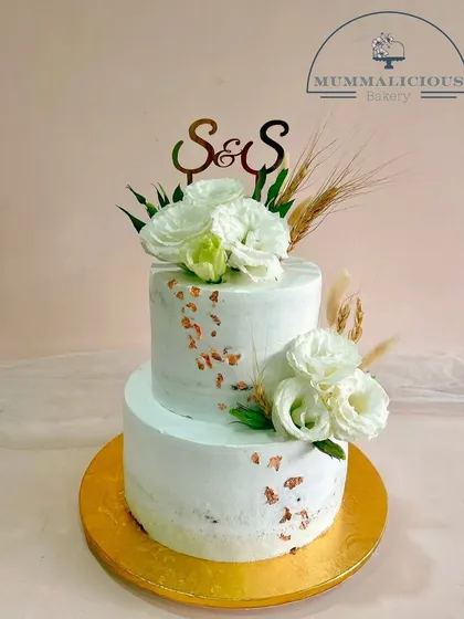 Rustic charm meets modern elegance in this two-tiered wedding cake. Adorned with simple white florals, wheat stalks, and a touch of gold leaf, it's perfect for a chic and understated celebration.