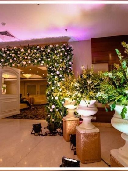 We ensure every corner of your venue is beautiful. This entrance is framed with a dense arch of white flowers, and large decorative urns filled with greenery add a touch of class to the lobby area.