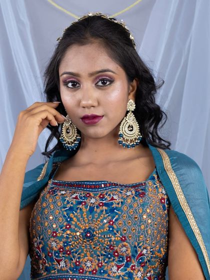 A close-up portrait highlighting the stunning, multi-color embroidery on the blouse and the large, matching statement earrings.