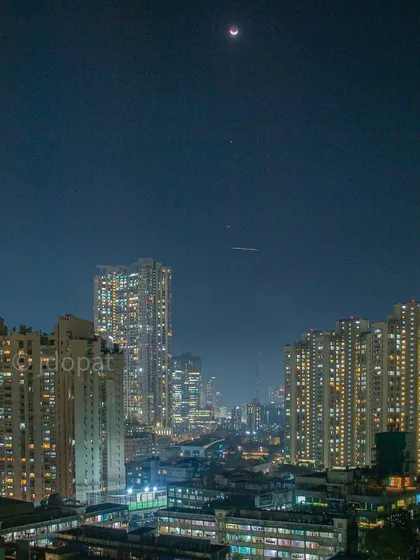 A wide shot of the celestial alignment over Mumbai, also capturing the light trail of a passing airplane.