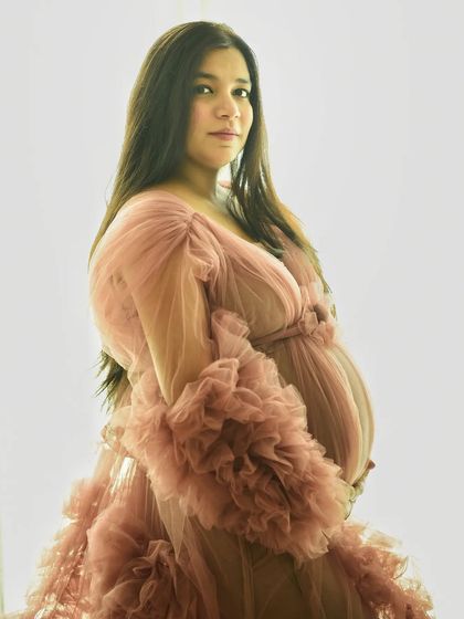 A simple, beautiful portrait against a clean white background. The soft pink gown and the mom-to-be's natural glow are the stars of the show.