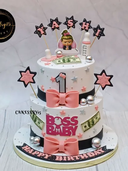 A stylish two-tier "Lady Boss" themed cake for a first birthday. This design uses a pink, black, and white color scheme with cute bows and star accents.
