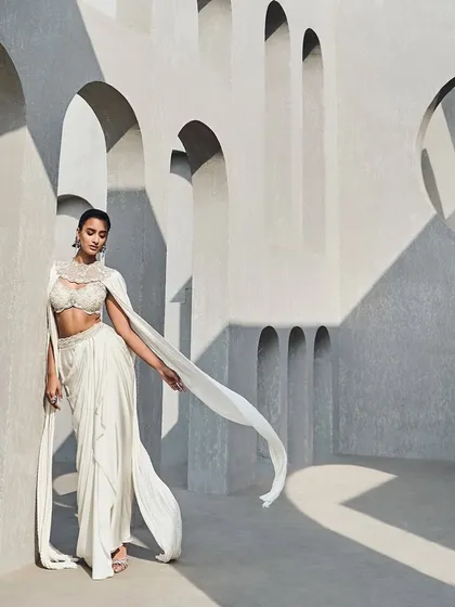 Here, I played with the idea of quiet drama. This ivory ensemble features a hand-embellished bustier and a cinched drape skirt, but the focus is the dramatic, floor-sweeping cape sleeves in crushed fabric. It is a study in structure and drape, designed for the modern muse.