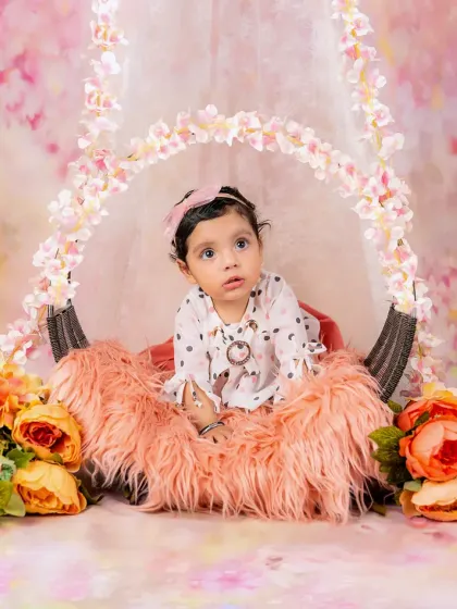 A baby girl looks up with a curious expression from her cozy spot in a beautiful floral swing prop.