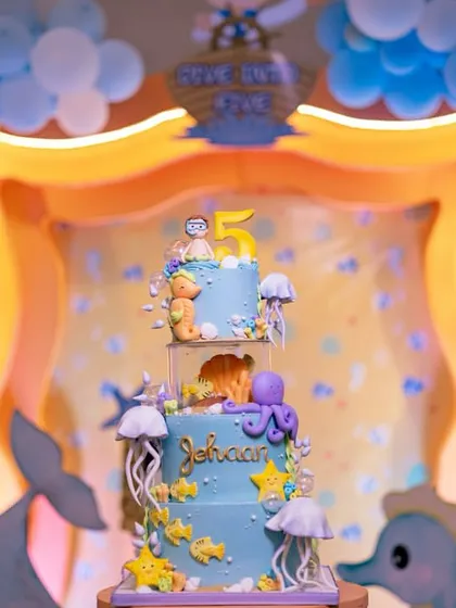 The birthday cake is the centerpiece of the celebration. This three-tiered 'Under the Sea' cake was designed to perfectly match the party's decor, complete with handcrafted sea creatures, coral, and a big number '5' on top.